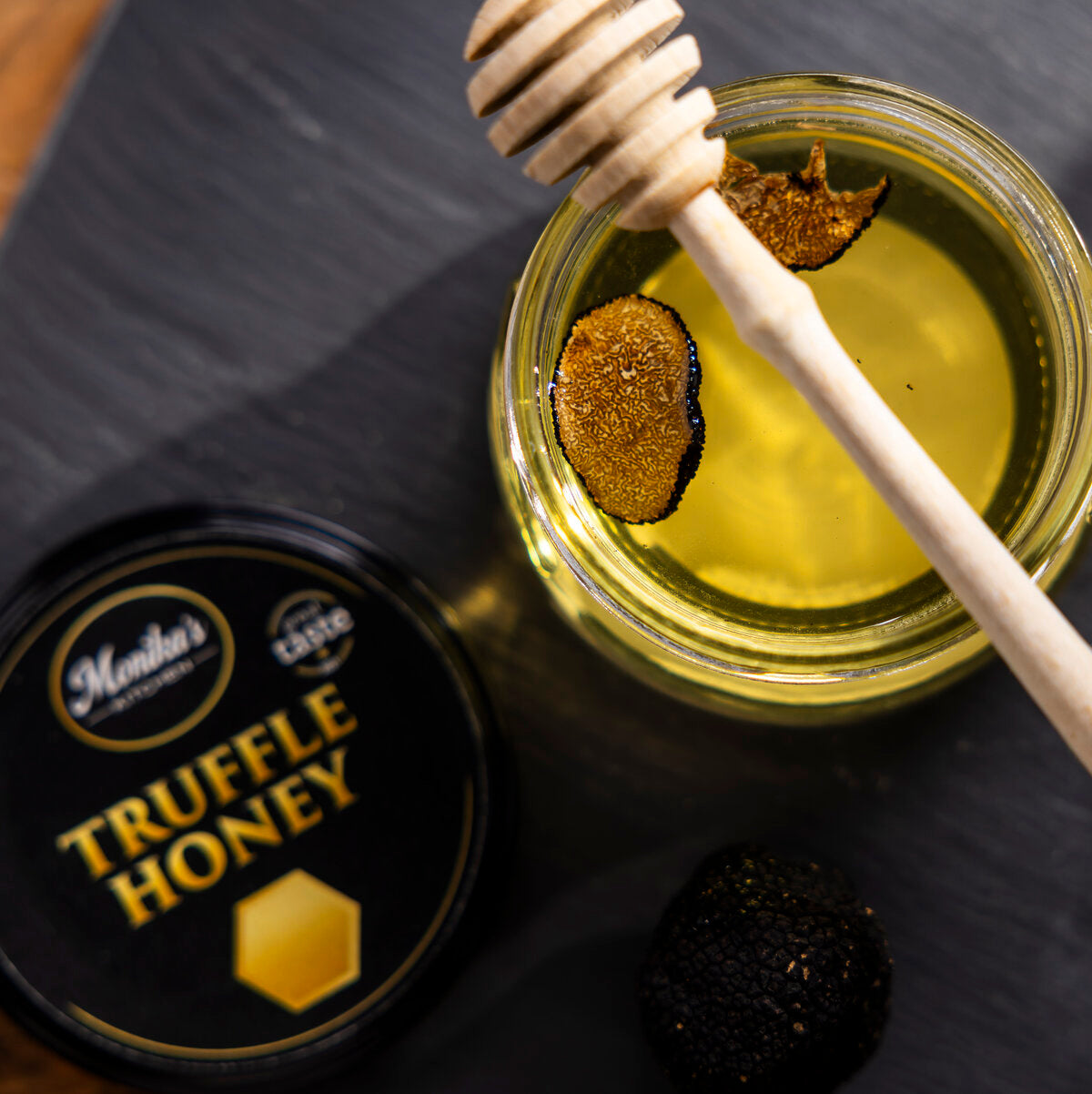 Jar of truffle honey infused with slices of black summer truffles, with a honey dipper.