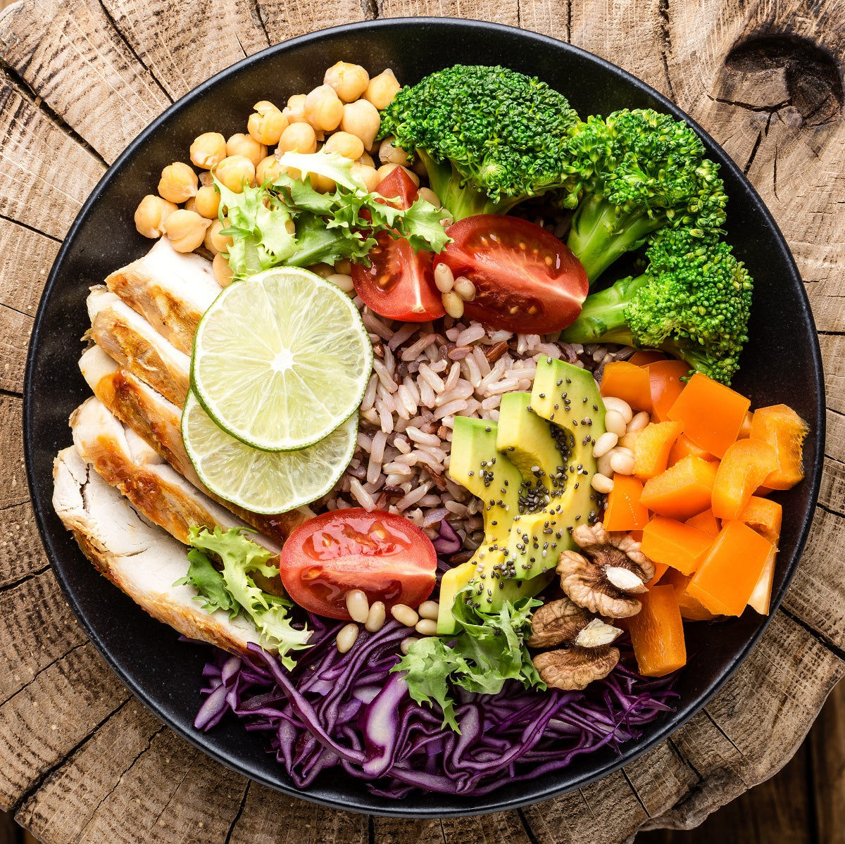 Healthy brown rice salad recipe with chicken, avocado, pepper, tomato, broccoli, cabbage, chickpea, lettuce, and walnuts.