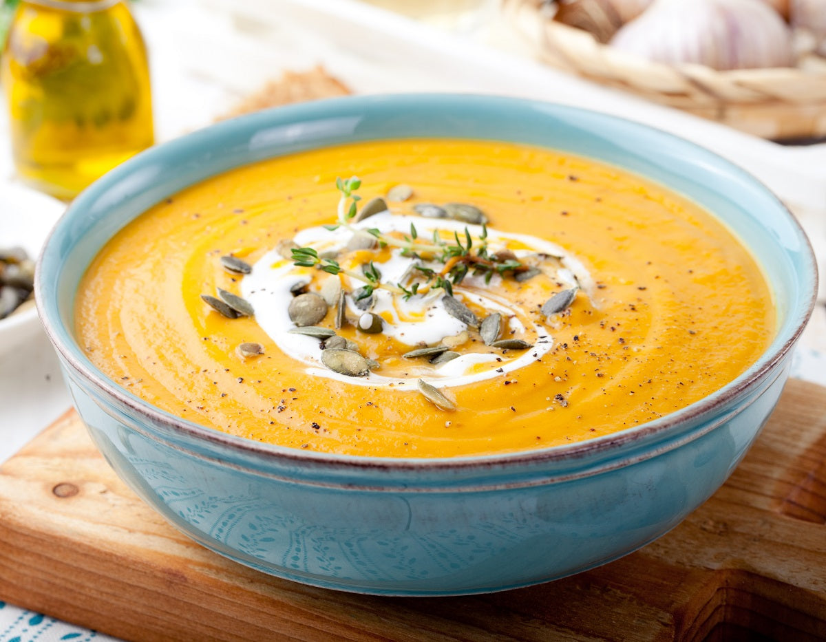 A bowl of healthy butternut squash soup recipe with a drizzle of pumpkin seed oil and a handful of seeds.