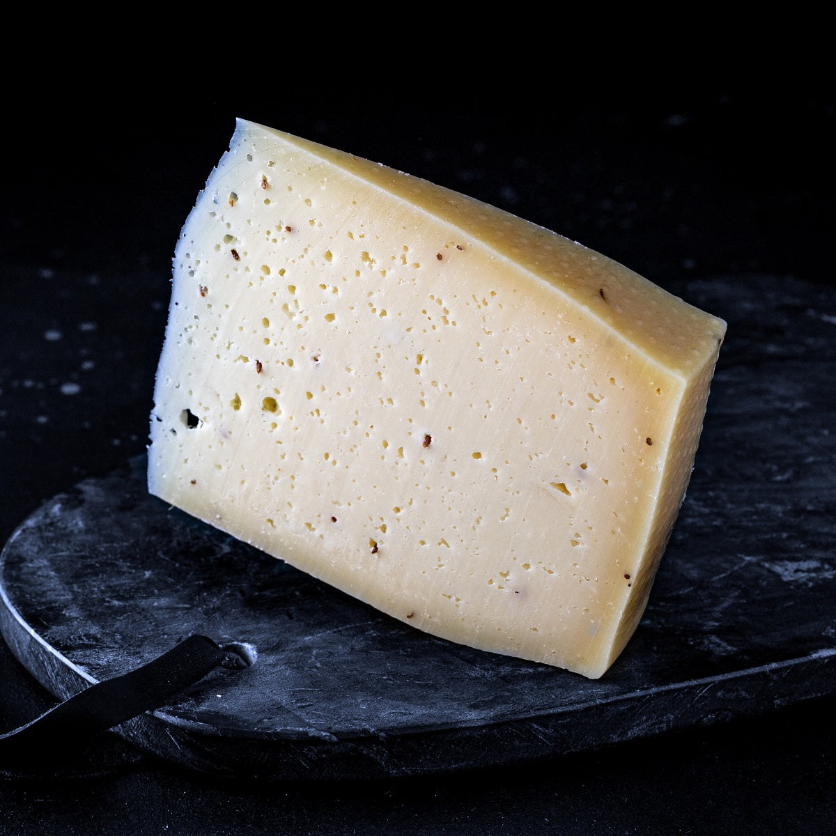 Gouda-style semi-hard artisan cow's cheese with whole caraway seeds on a white background.