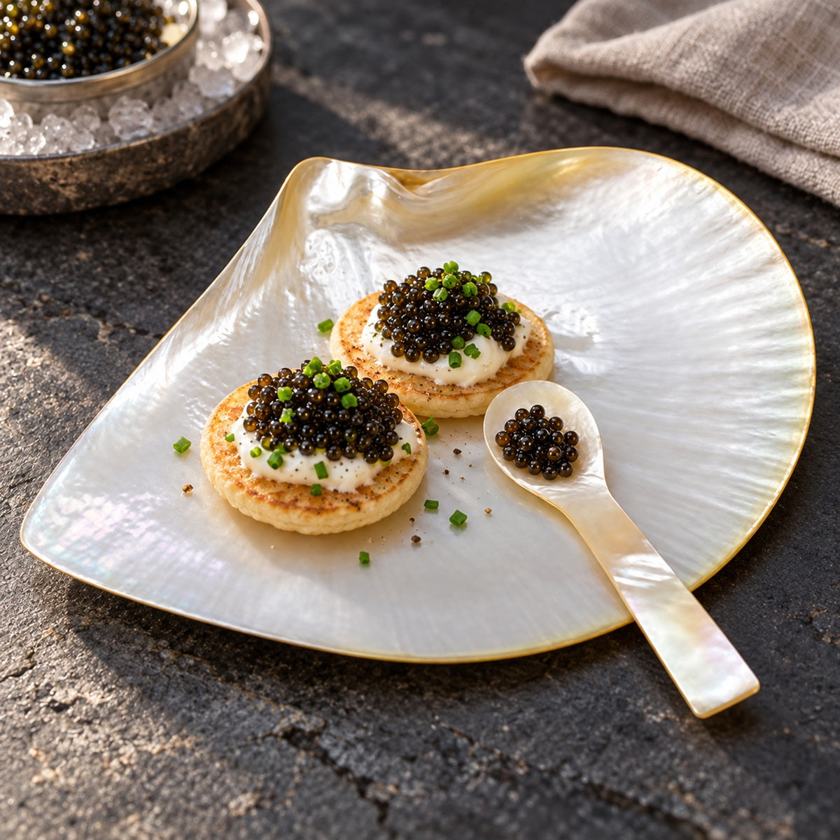 Black caviar on blinis, served on a handmade mother-of-pearl caviar plate with a mother-of-pearl spoon.