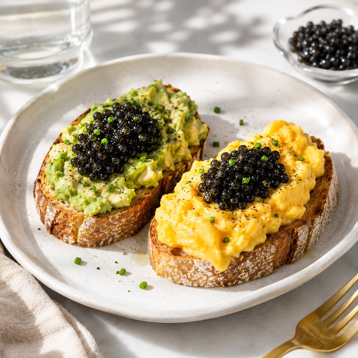 Two pieces of toast, one with avocado and the other with scrambled eggs, both topped with caviar.