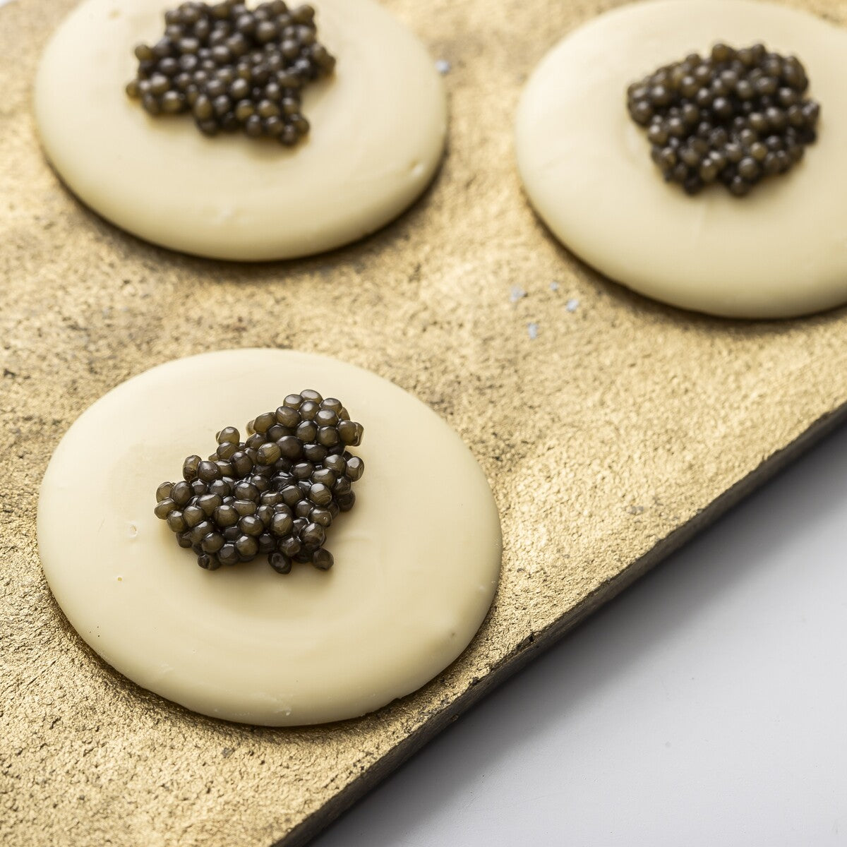 Black caviar from the the best fish egg roe served on white chocolate buttons for a gourmet experience.