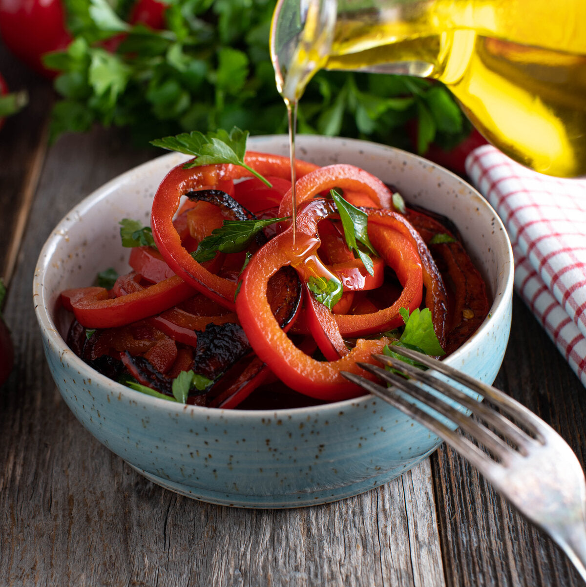 Salad in a blue bowl with a fork, drizzled with flaxseed oil on a wooden surface.