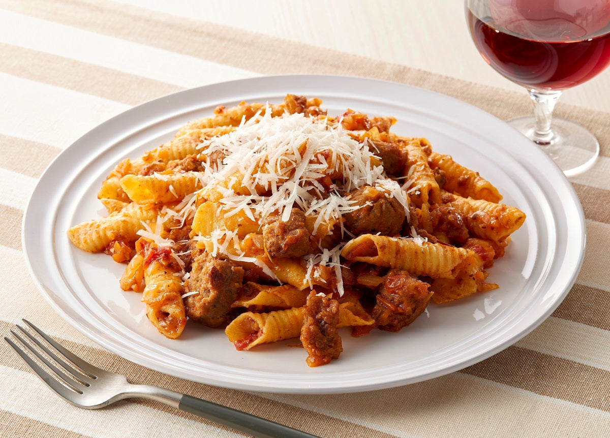 A plate of garganelli pasta with a Bolognese ragu sauce and a glass of red wine.