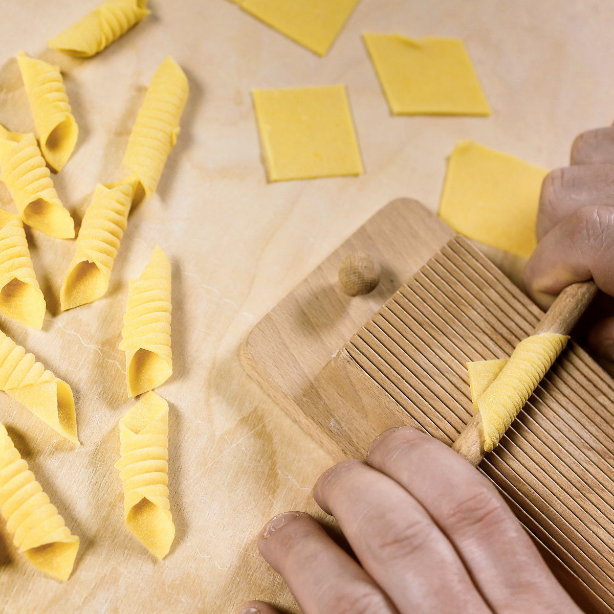 Fresh Garganelli pasta being hand-rolled using a wooden pasta maker machine.
