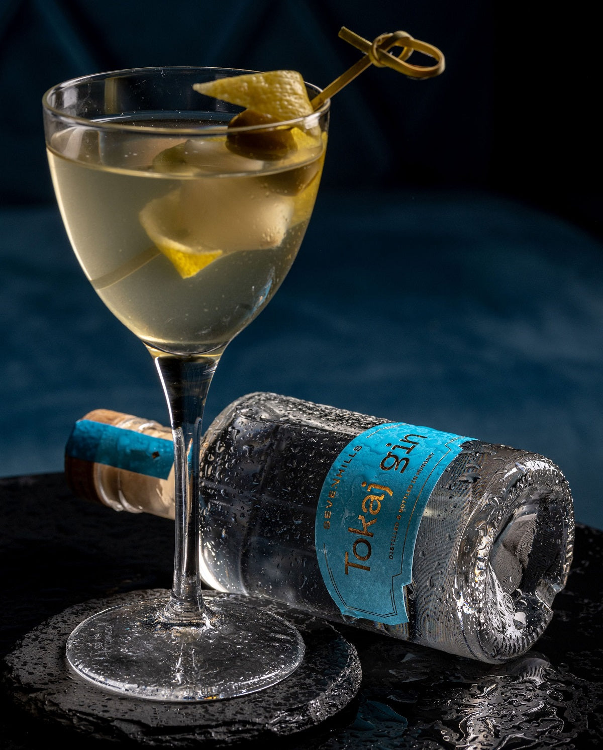 A glass of gin and tonic cocktail with lemon peel and olive.