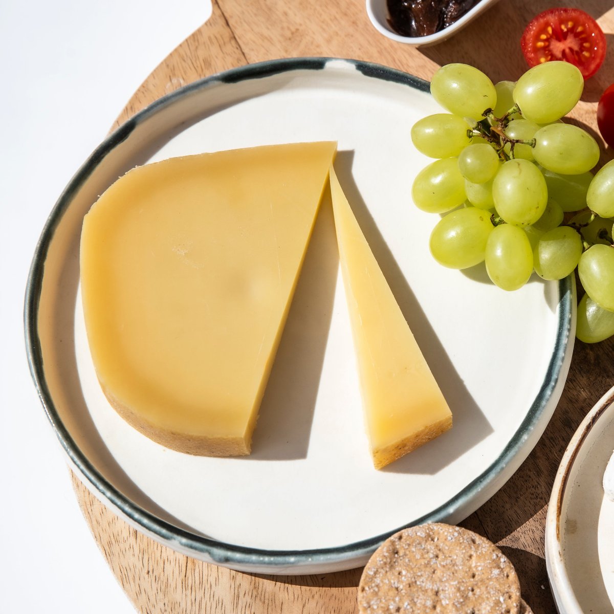 A piece of Gouda-style semi-hard cheese on a plate with grapes and crackers.