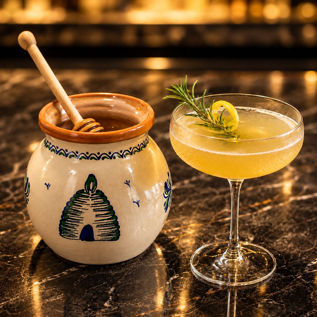Honey cocktail in a glass with a lemon twist next to honey in a pot on a dark surface.