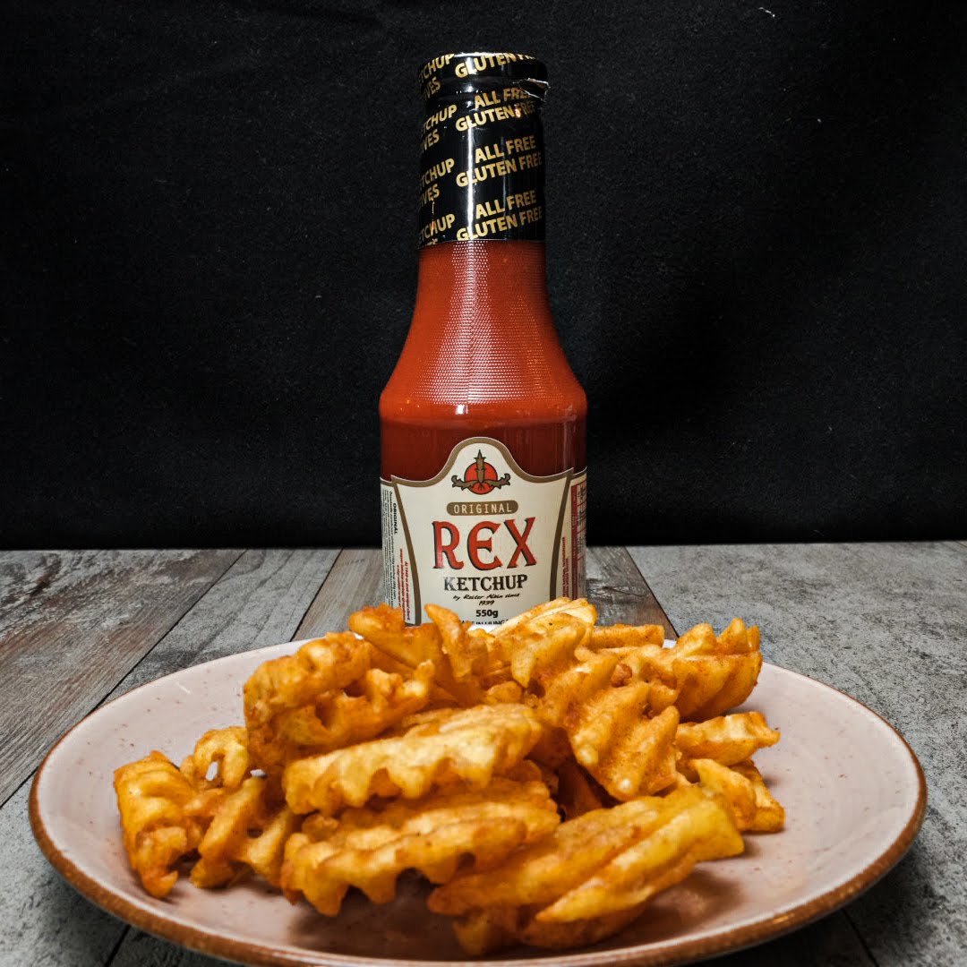 A bottle of tomato ketchup with a plate of potato fries chips.