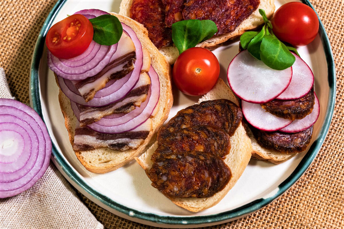 Slices of mangalitza chorizo sausage on bread with tomatoes and red onion.