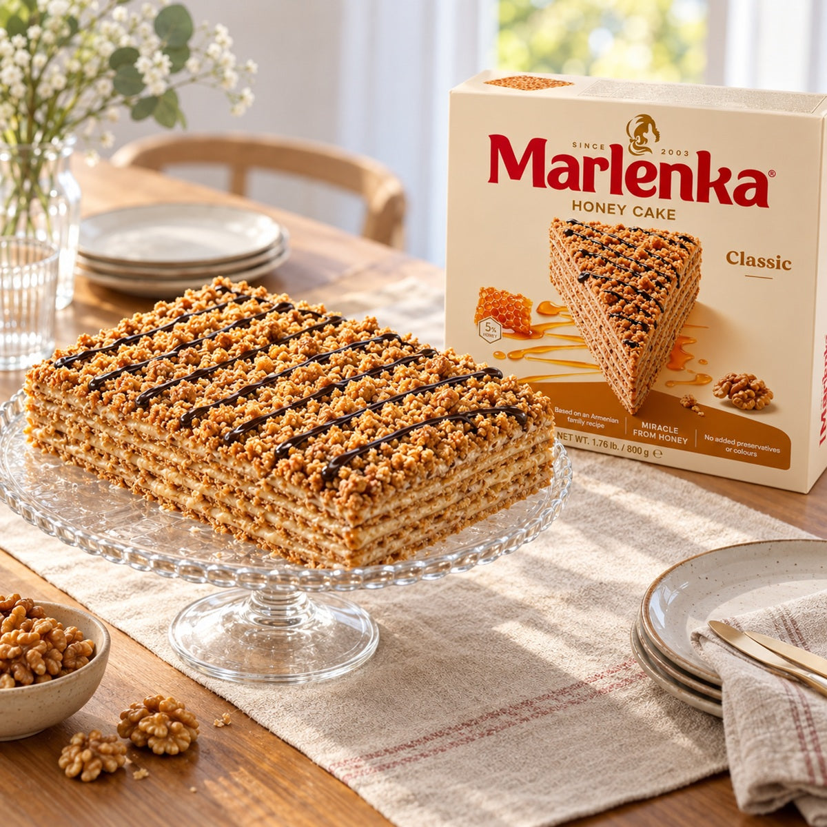 A whole piece of Marlenka Honey Cake on a cake stand with a box of Marlenka Classic Honey Cake in the background.