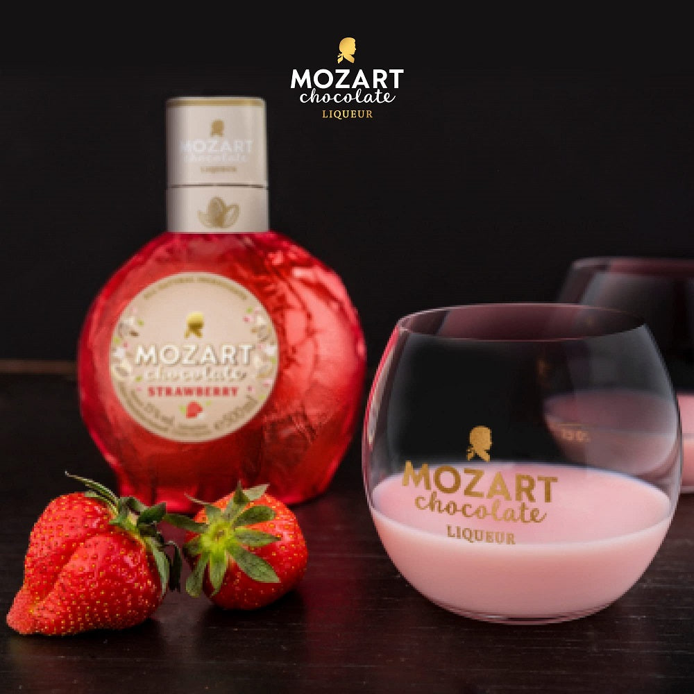 A bottle and a glass of Mozart white chocolate liquor with fresh strawberries.