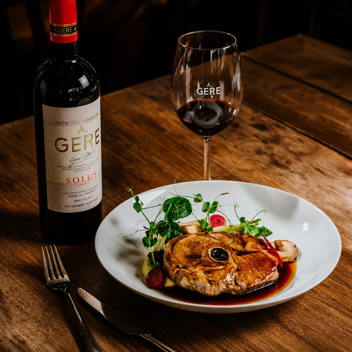 A plate of osso buco with vegetables and jus, paired with a bottle of Merlot red wine.