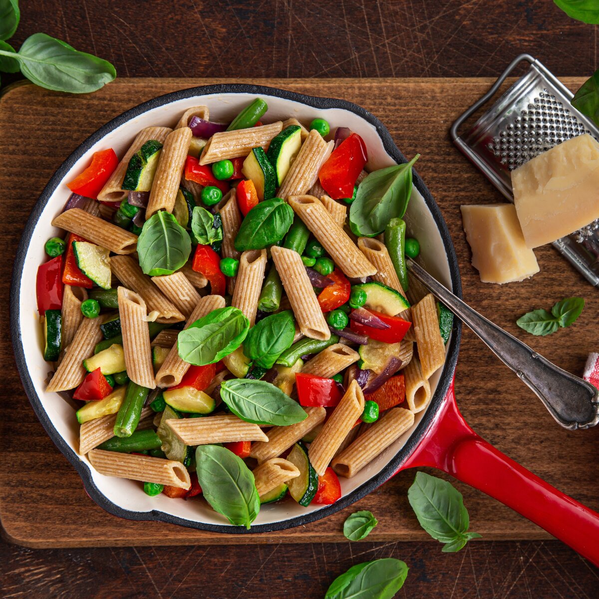 A bowl of penne pasta made from plantain flour, served with grilled vegetables and cheese.