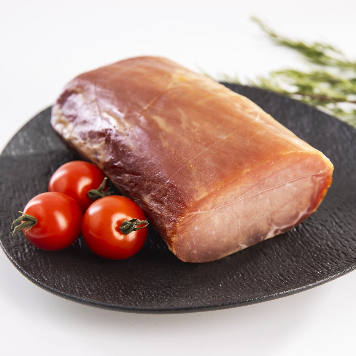 A cold-smoked loin of pork from fillet meat with tomatoes on a plate.