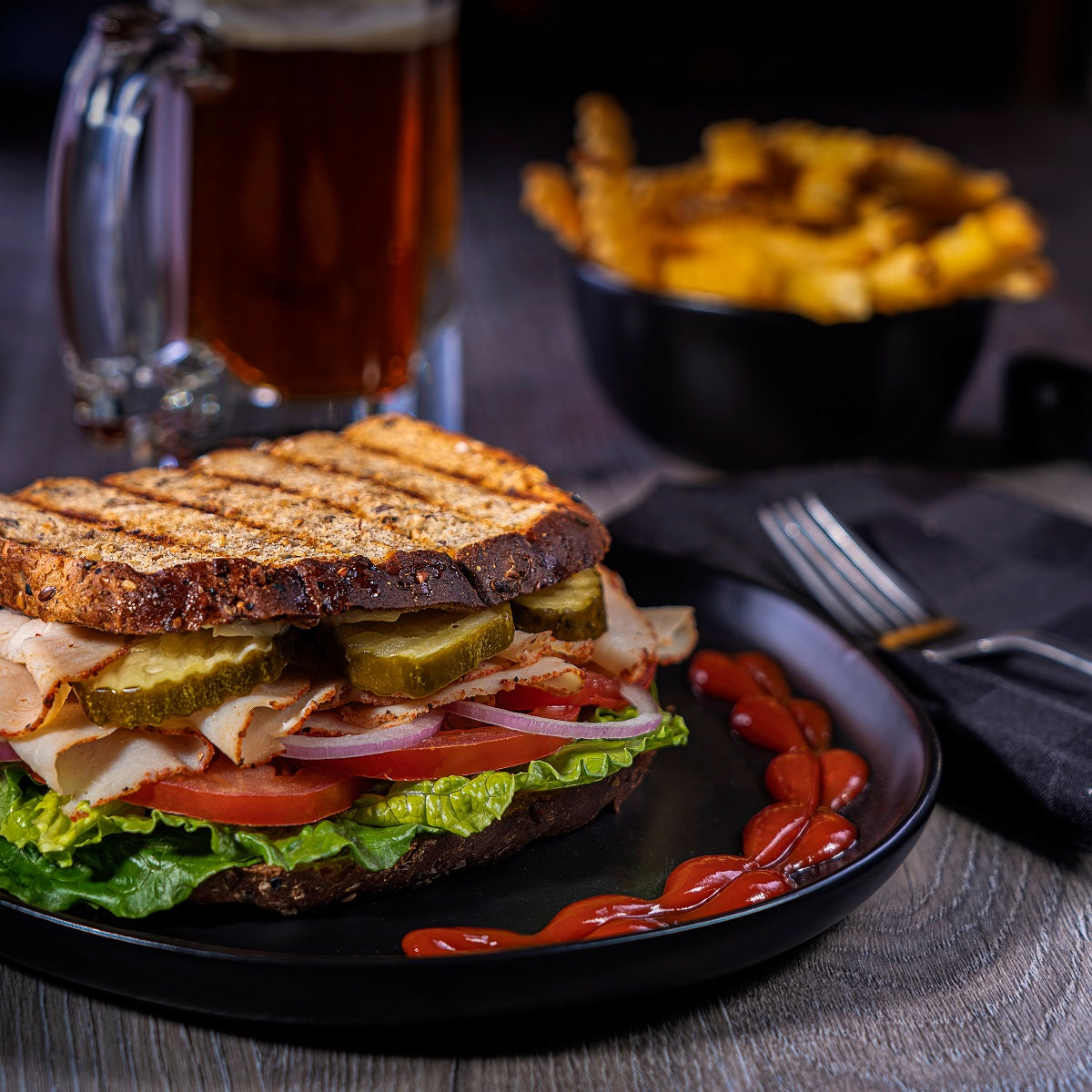 Grilled sandwich with vegetables and spicy ketchup, accompanied by French fries and a beer.