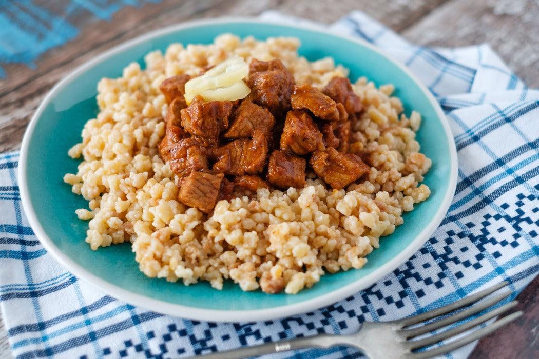 A plate of traditional Hungarian beef stew with a side dish of tarhonya pasta.
