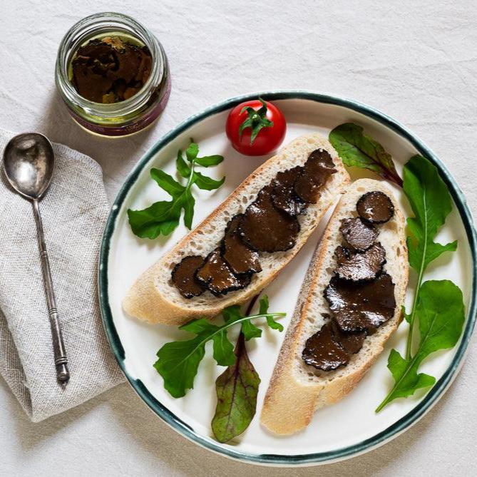 Black truffle carpaccio slices in oil, served on toasted bread with rocket leaves and tomato.