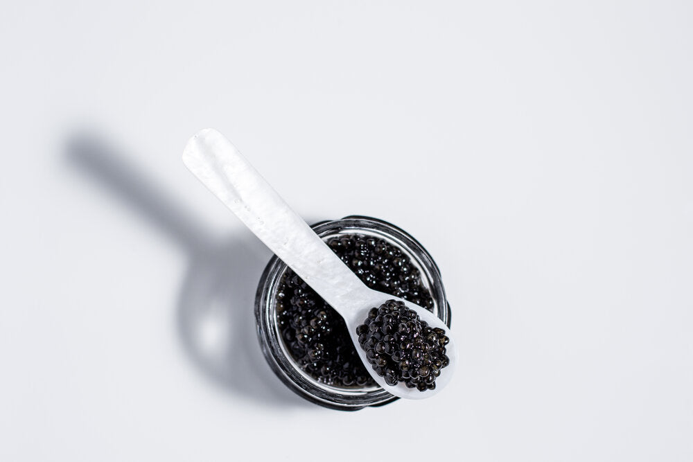An open tin of black caviar with a mother of pearl serving spoon.