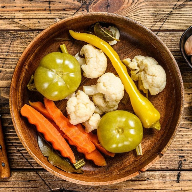 Mixed assorted artisan pickled vegetables including carrots, peppers, cauliflower and green tomatoes.