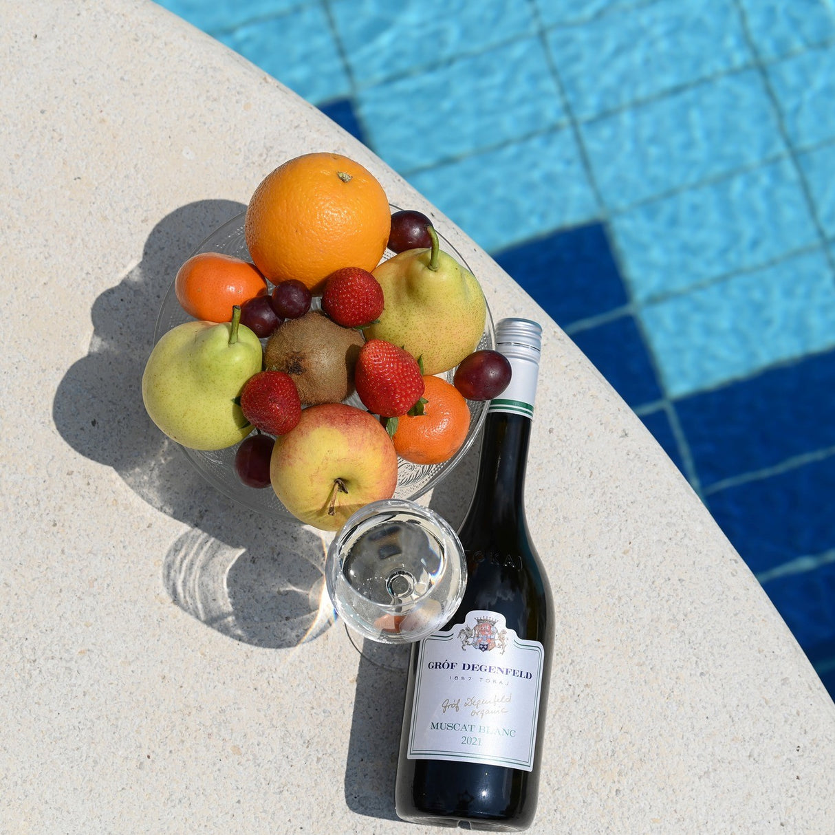 A bottle of off-dry Muscat Blanc white wine with a bowl of fruit by the side of the swimming pool.