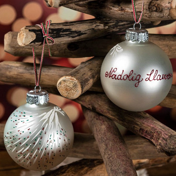 A Welsh Christmas tree bauble with the hand-painted greeting "Nadolig Llawen" for wishing a Merry Christmas.