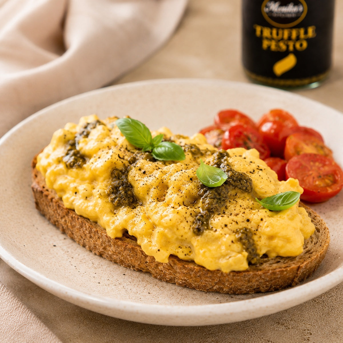 Scrambled eggs on toast, topped with truffle pesto, with cherry tomatoes on the side.