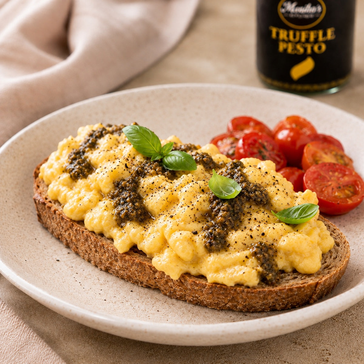 Scrambled eggs on toast, topped with truffle pesto, with cherry tomatoes on the side.