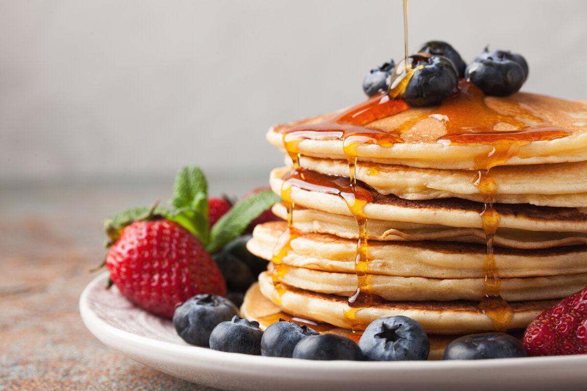 A stack of pancakes with berries and a drizzle of the best raw natural wildflower honey.