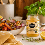Jar of Monika's Kitchen Acacia Honey on a table with roasted vegetables and lemons.