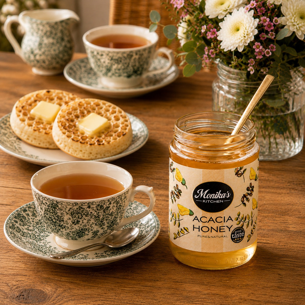 Tea cups with crumpets and a jar of acacia honey on a wooden table.