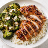 Plate of roasted chicken coated in an apricot balsamic vinegar glaze, served on a bed of rice with roasted broccoli.