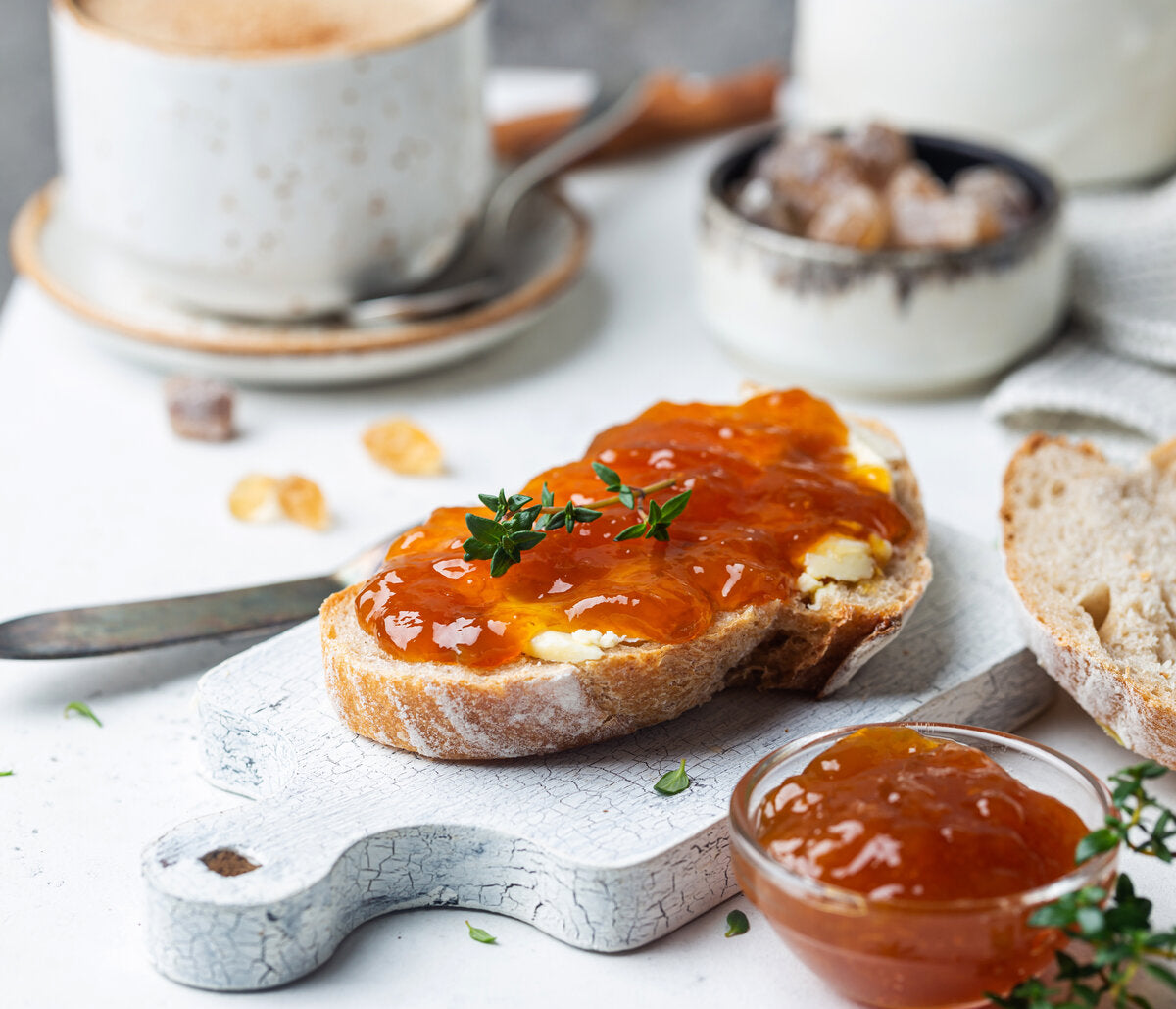 Slice of toast with apricot jam and a cup of coffee in the background.
