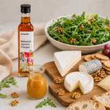 Balsamic Apricot Vinegar bottle with a small jar of dressing on a wooden board with cheese, bread, and salad.