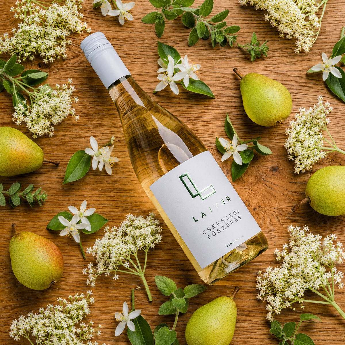 A bottle of white wine from the aromatic Cserszegi Fűszeres grape surrounded by pears and fragrant flowers.