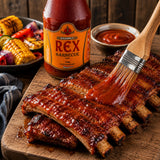 Grilled ribs being brushed with BBQ Ketchup to form a glaze, on a wooden cutting board.