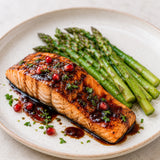 Salmon dish with a pomegranate balsamic vinegar glaze and a side of steamed asparagus on a white plate.