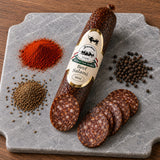 Slices of beef salami on a marble board next to the whole salami and spices.