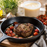 Steak fried in beef tallow, with roasted cherry tomatoes in a frying pan, and a tub of beef tallow in the background.