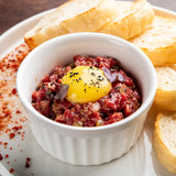 Beef tartare with an egg yolk on top, sprinkled with smoked ground black pepper.