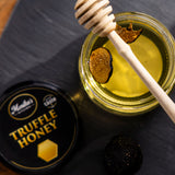 Jar of truffle honey infused with slices of black summer truffles, with a honey dipper.