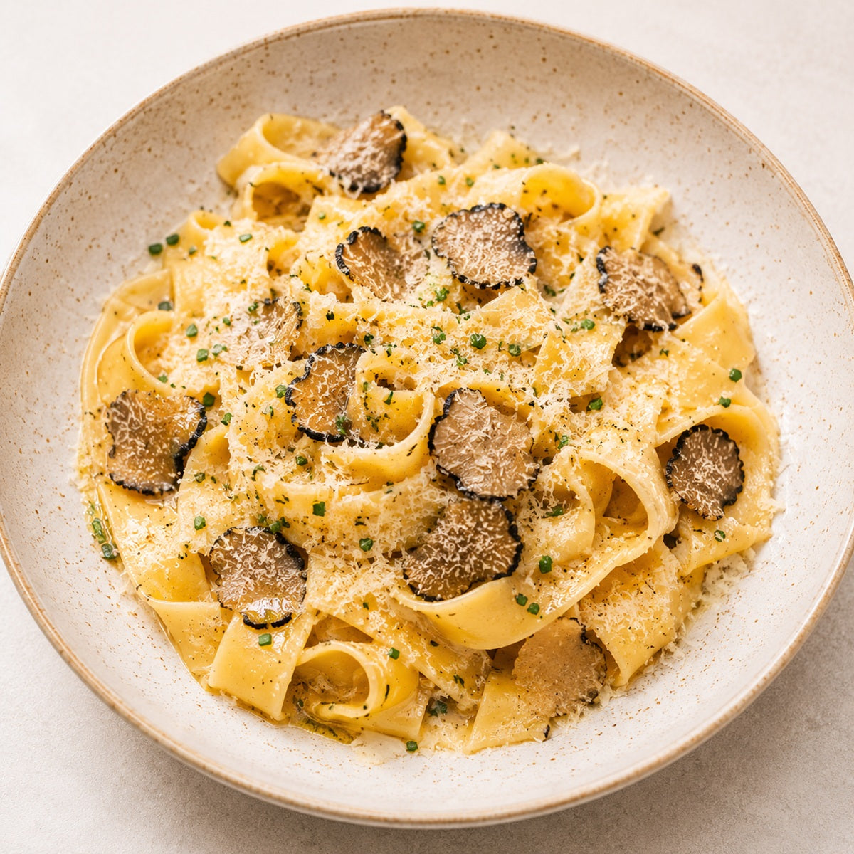 Plate of truffle pasta with slices of black truffle, grated parmesan and fresh herbs.