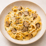 Plate of truffle pasta with slices of black truffle, grated parmesan and fresh herbs.