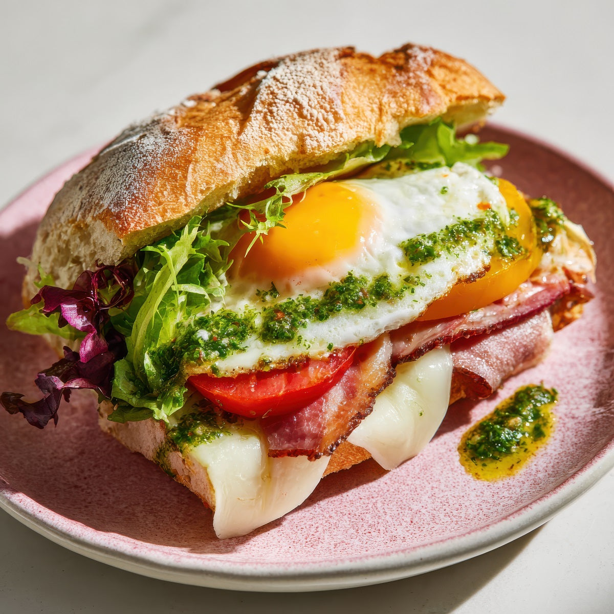 Breakfast sandwich with egg, ham, and vegetables on a pink plate