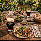 Outdoor dining scene with plates of food, glasses of cascara cola, and cutlery on a wooden table.