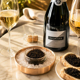 Bottle of Champagne wine with two glasses and a dish of caviar on a marble surface.
