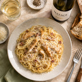Plate of spaghetti carbonara pasta with chicken, paired with a bottle of Chardonnay wine and glasses on a table.