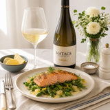 Salmon dish with white wine, bottle of Chardonnay, and flowers on a table.