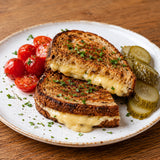 Grilled cheese sandwich made with rye bread and Gouda cheese with caraway seeds, served with tomatoes and pickles.